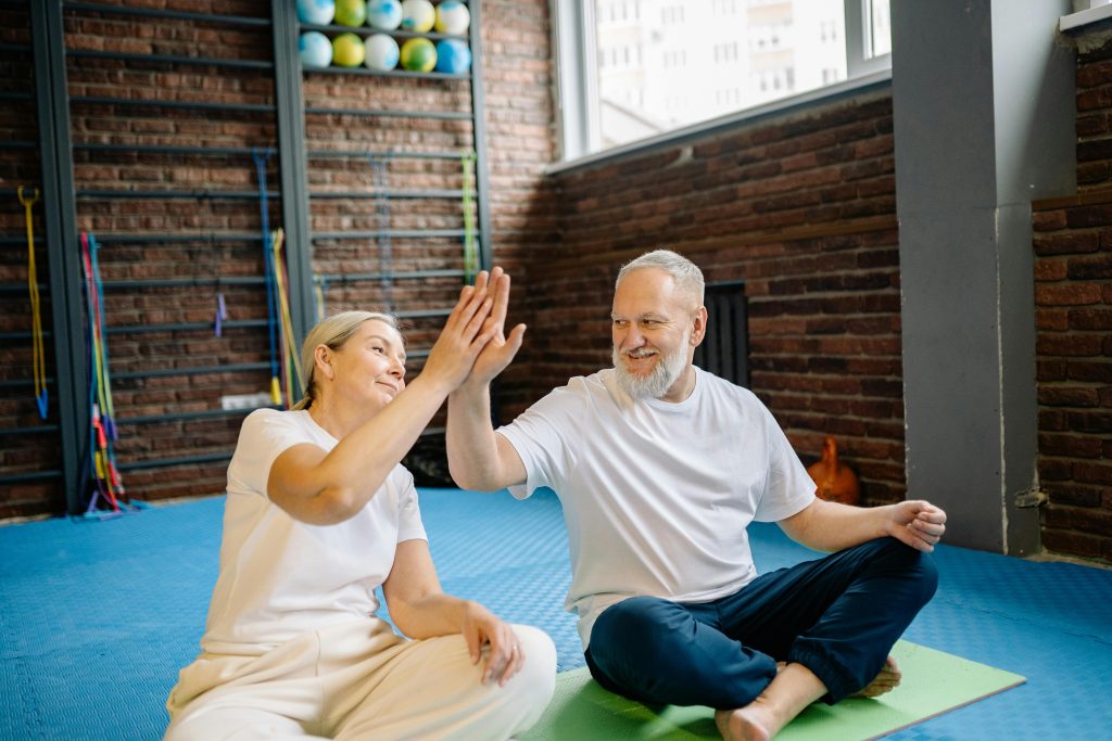 pexels-photo-6815703-6815703 Energetic senior couple enjoying yoga, sharing a joyful high-five at the gym.