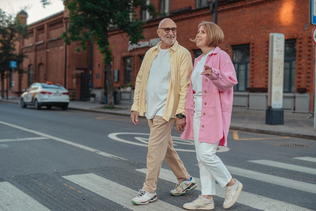 pexels-photo-8972269-8972269 Happy senior couple walking hand in hand across a city pedestrian crossing.